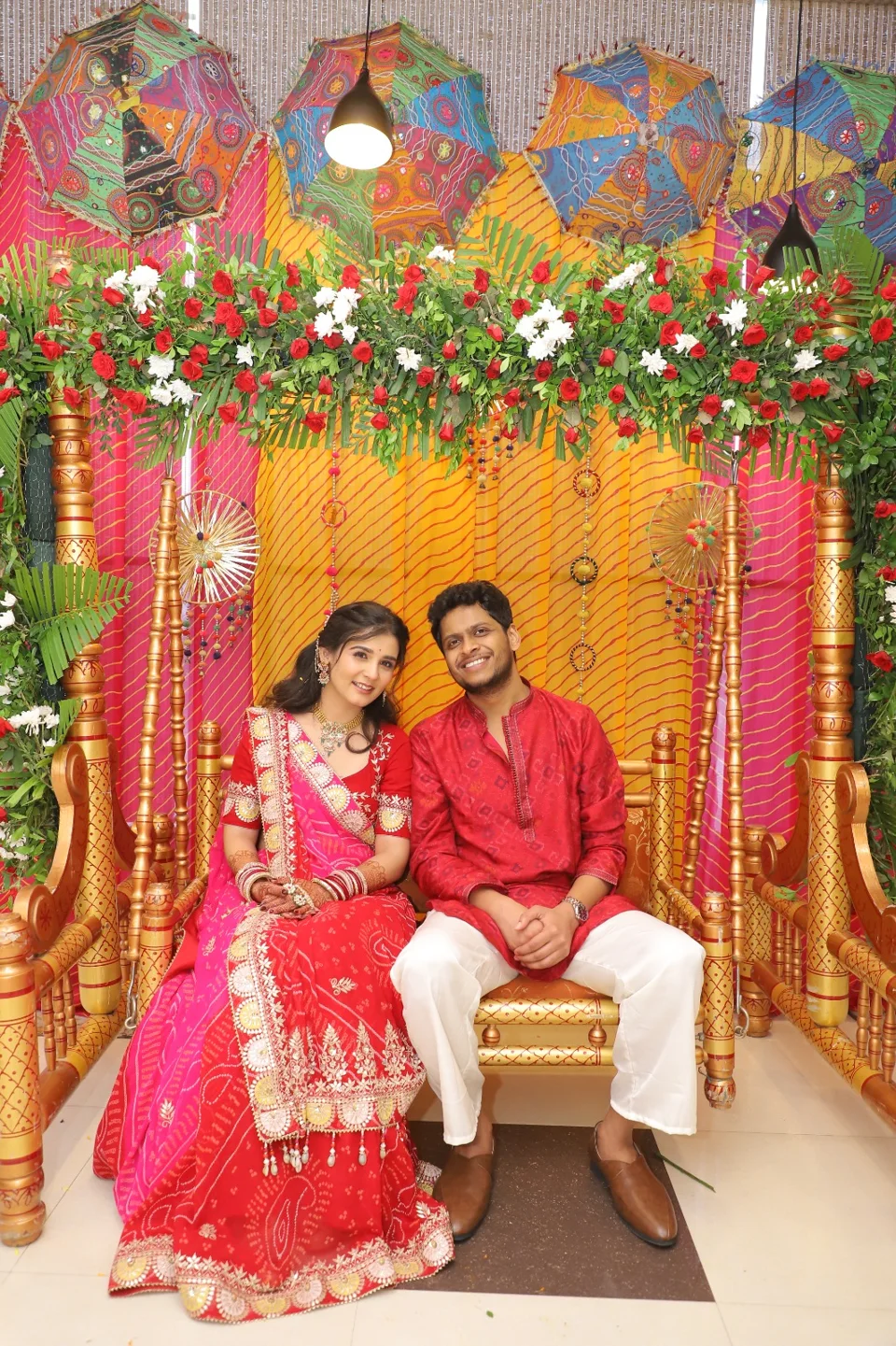 Vishal and Shruti seated together beneath colourful flowers and umbrellas